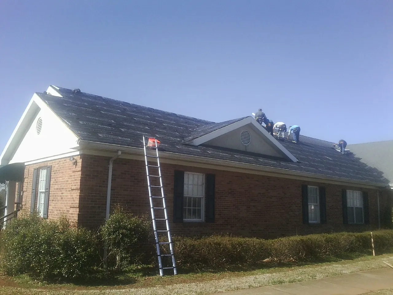 Crew tearing shingles off a brick ranch roof with a ladder set — Metal Roof Repair work by our crew in Templeton