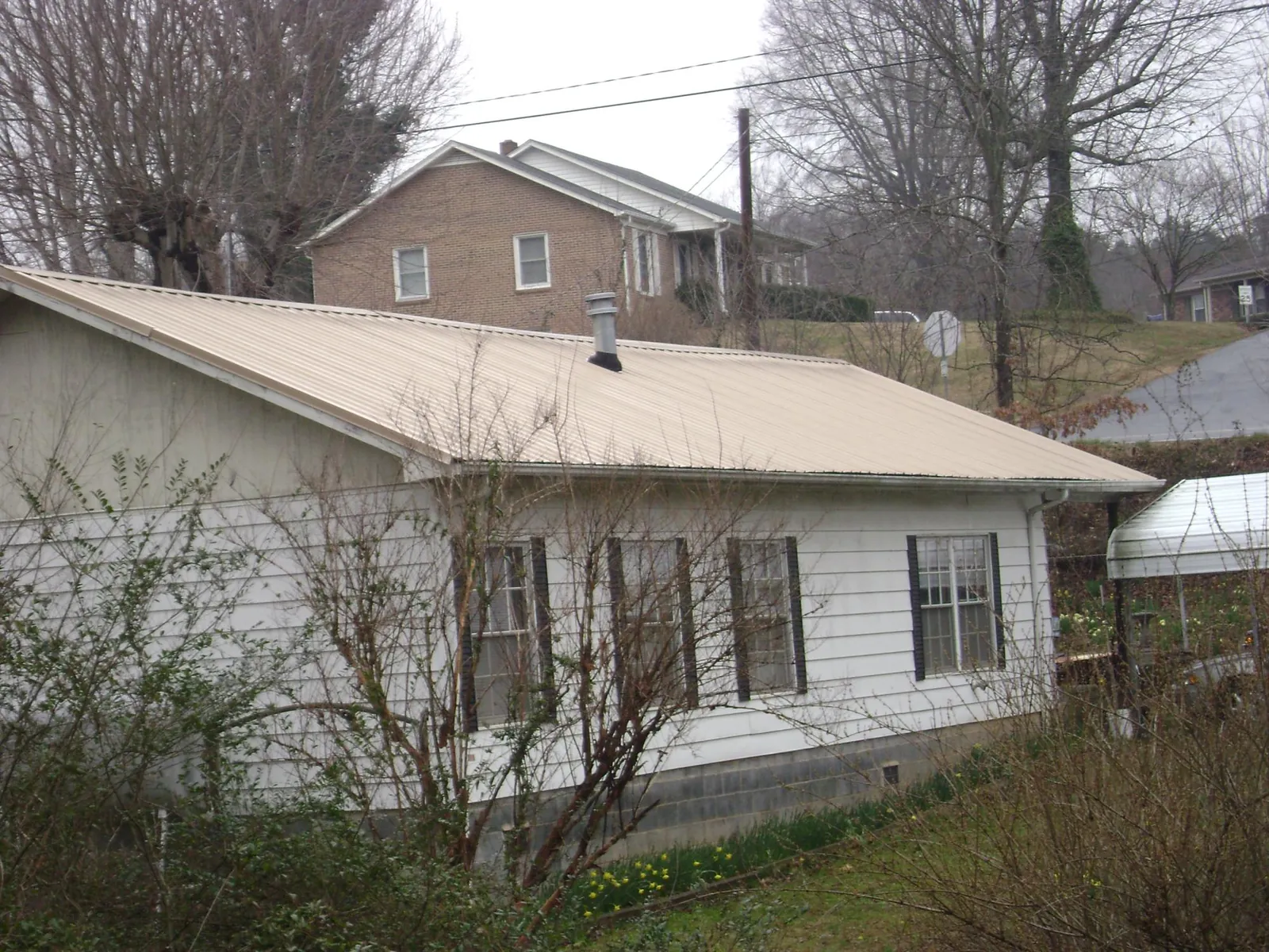 Tan metal roof on a white sided house set into a hillside — Commercial Roofing by Roofing Brothers in Templeton